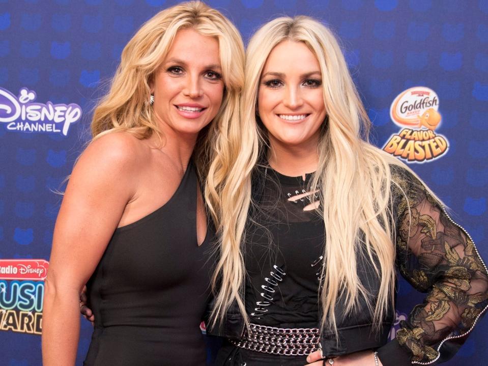 Britney and Jamie Lynn in black ensembles in front of a Disney backdrop.