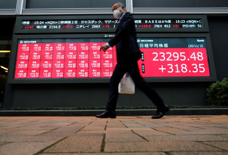 A man wearing a protective face mask walks past a stock quotation board outside a brokerage, amid the coronavirus disease (COVID-19) outbreak, in Tokyo