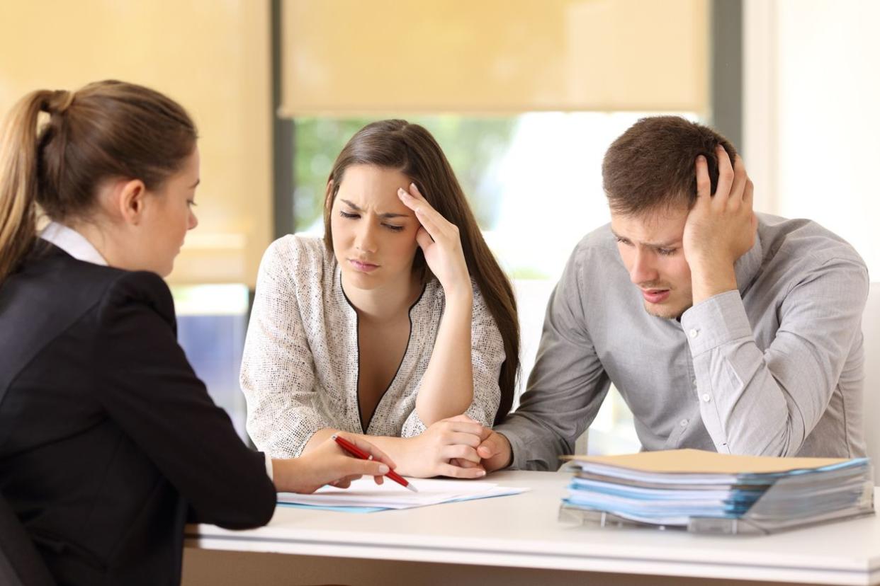 Saleswoman explaining conditions of a document with bad news to a couple of worried customers at office