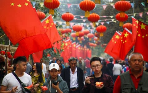 People walk under Chinese national flags in the Old City in Kashgar in Xinjiang - Credit: REUTERS/Thomas Peter