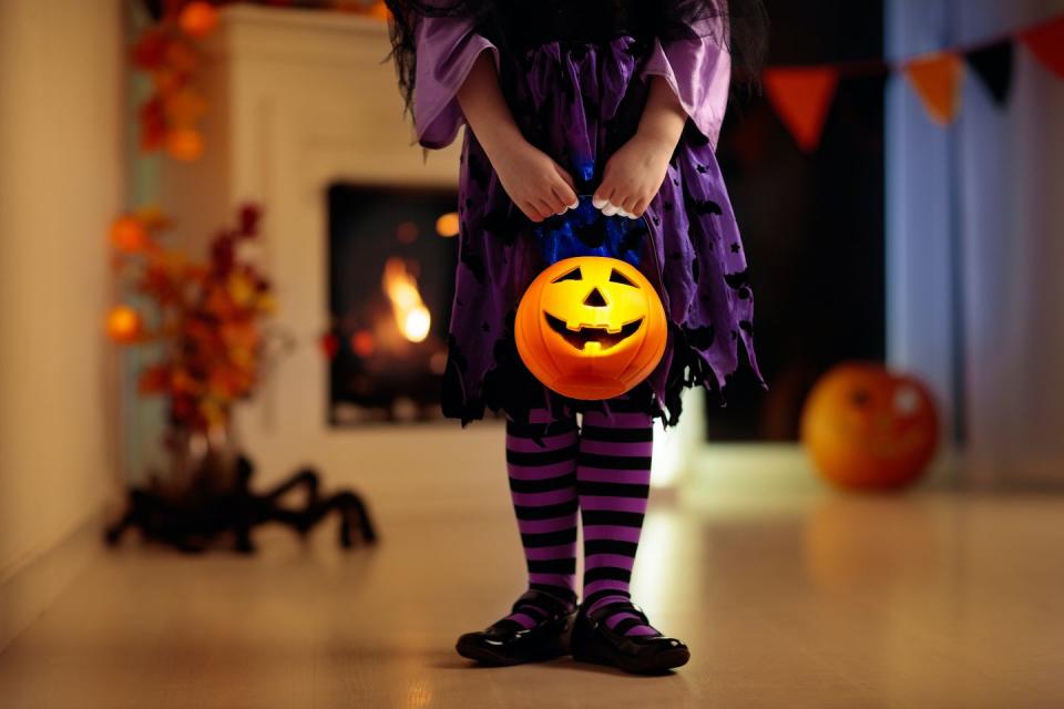 little girl in witch costume on halloween trick or treat at home pumpkin and candle decoration of fireplace dressed up child trick or treating kid holding candy bucket kids celebrate halloween