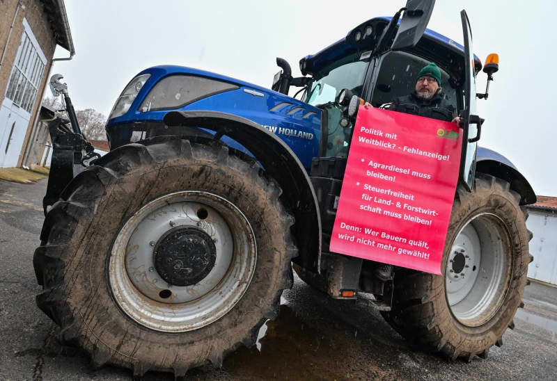 Frank Schuhmacher, Production Manager at Landgesellschaft Lebus GmbH, holds a banner in front of his tractor during a protest by farmers against the planned cuts and cuts by the federal government. Patrick Pleul/dpa