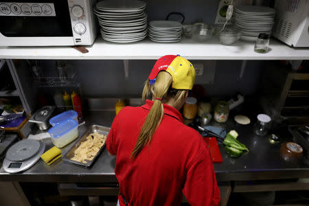 Fiamma, a Venezuelan worker in Spain, wears a cap in the national Venezuelan colours as she cuts vegetables inside a Venezuelan traditional food restaurant in Madrid, Spain, May 16, 2018. REUTERS/Sergio Perez