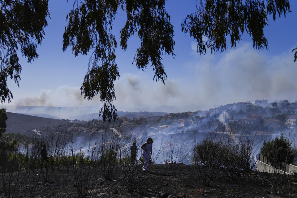 A woman walks in front of smoke from a fire in the area of Drafi , east of Athens on Wednesday, July 20, 2022. Hundreds of people were evacuated from their homes late Tuesday as a wildfire threatened mountainside suburbs northeast of Athens. Firefighters battled through the night, struggling to contain the blaze which was being intensified by strong gusts of wind. (AP Photo/Thanassis Stavrakis)