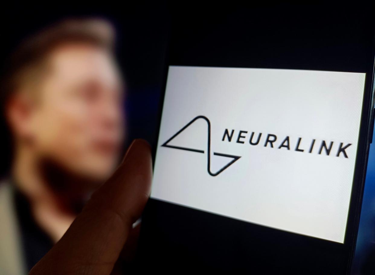 Neuralink logo displayed on a screen with a blurred image of Elon Musk behind it.