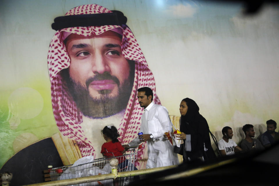 A Saudi family walk past a giant poster of Saudi Crown Prince Mohammed bin Salman, at a shopping mall in Jiddah, Saudi Arabia, Sunday, Sept. 15, 2019. The weekend drone attack on one of the world's largest crude oil processing plants that dramatically cut into global oil supplies is the most visible sign yet of how Aramco's stability and security is directly linked to that of its owner -- the Saudi government and its ruling family. (AP Photo/Amr Nabil)