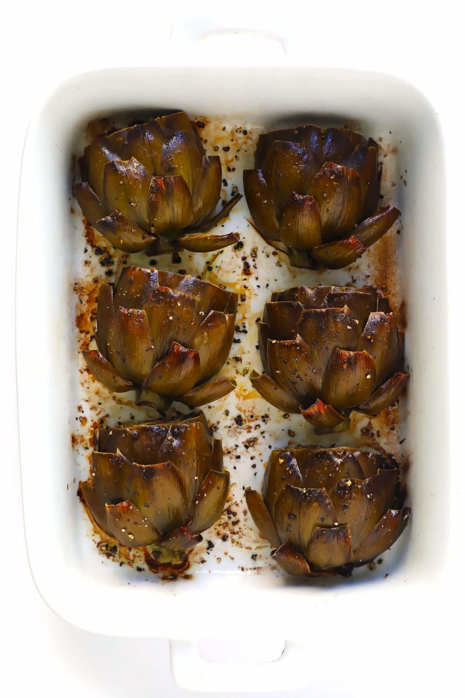 Four roasted artichokes in a white baking dish