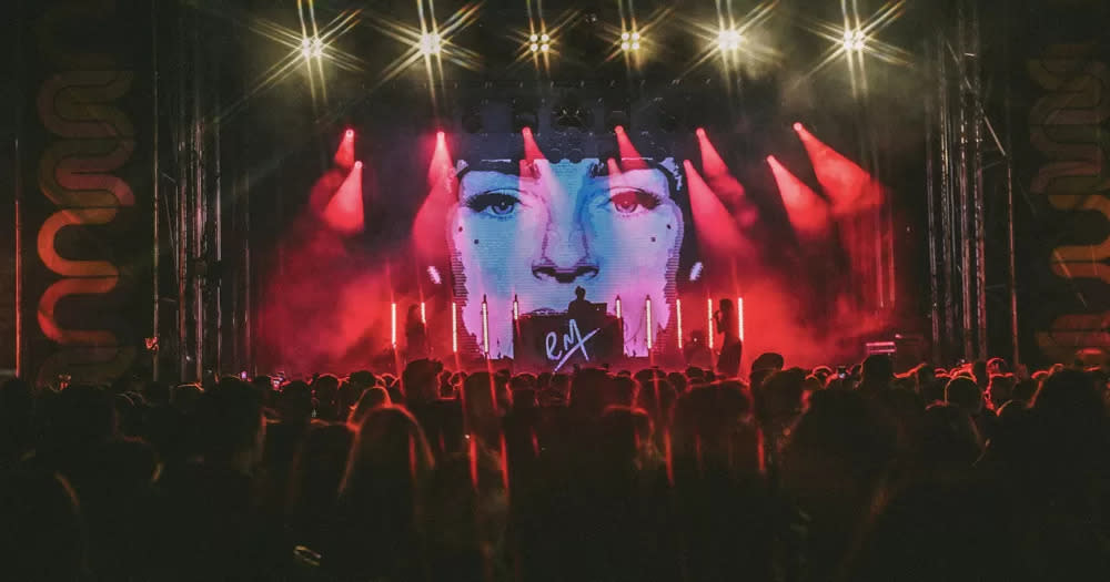 Photo from Mother's Cultur Club night in 2023, with people listening to DJ Elaine Maine on the stage, with red lights and a woman's face on the screen.