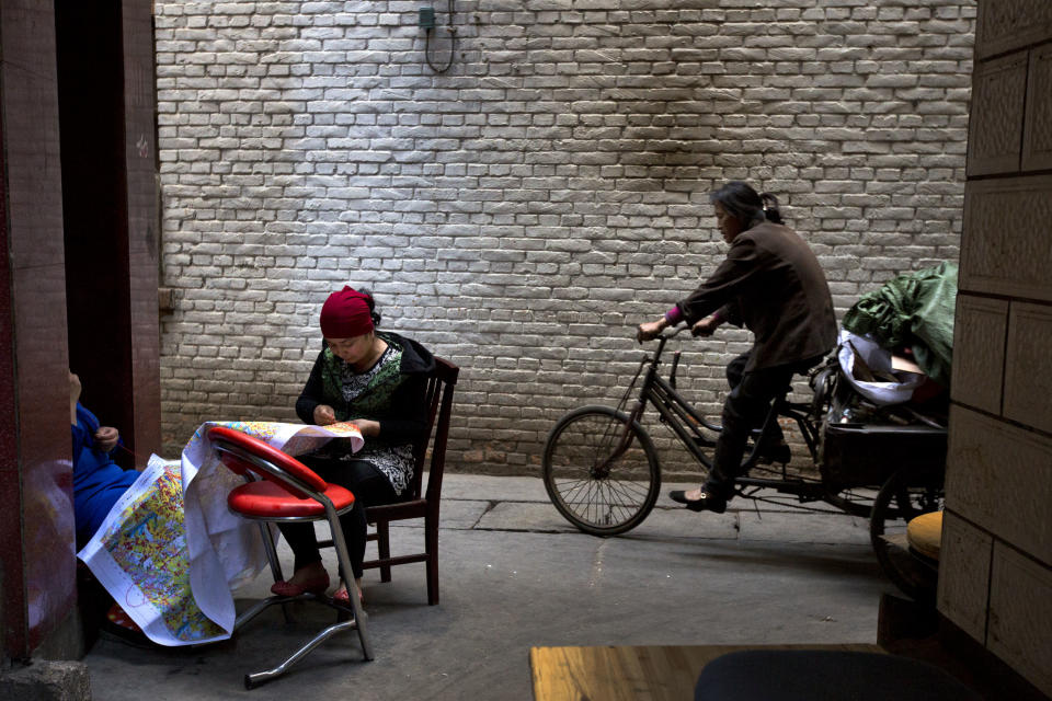 In this Sunday March 2, 2014 photo, Uighur women, left, sew as a Han Chinese woman rides her tricycle cart past them in a community shared by both Han Chinese and Uighur ethnic residents in Kunming, in southwestern China's Yunnan province. China said the vicious slashing spree Saturday that killed 29 people in the southern city was the work of separatists linked to international terrorism, but the assailants’ homespun methods and low-tech weapons - nothing more than long knives - have led some analysts to suspect they didn’t get outside help. (AP Photo/Alexander F. Yuan)