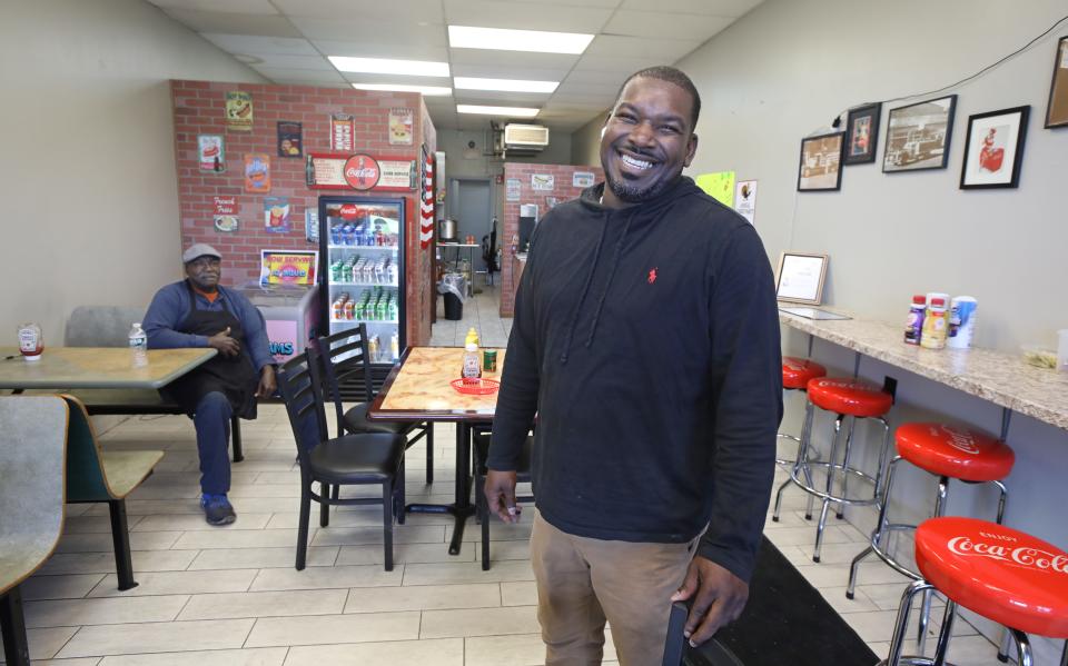 Cedric Scott stands in his newly opened Scott's Scottsville Hots in Scottsville Wednesday, Oct. 20, 2021.  Seated at back is Cedric's father, Roosevelt Scott, who comes in most mornings to help with the cooking. 