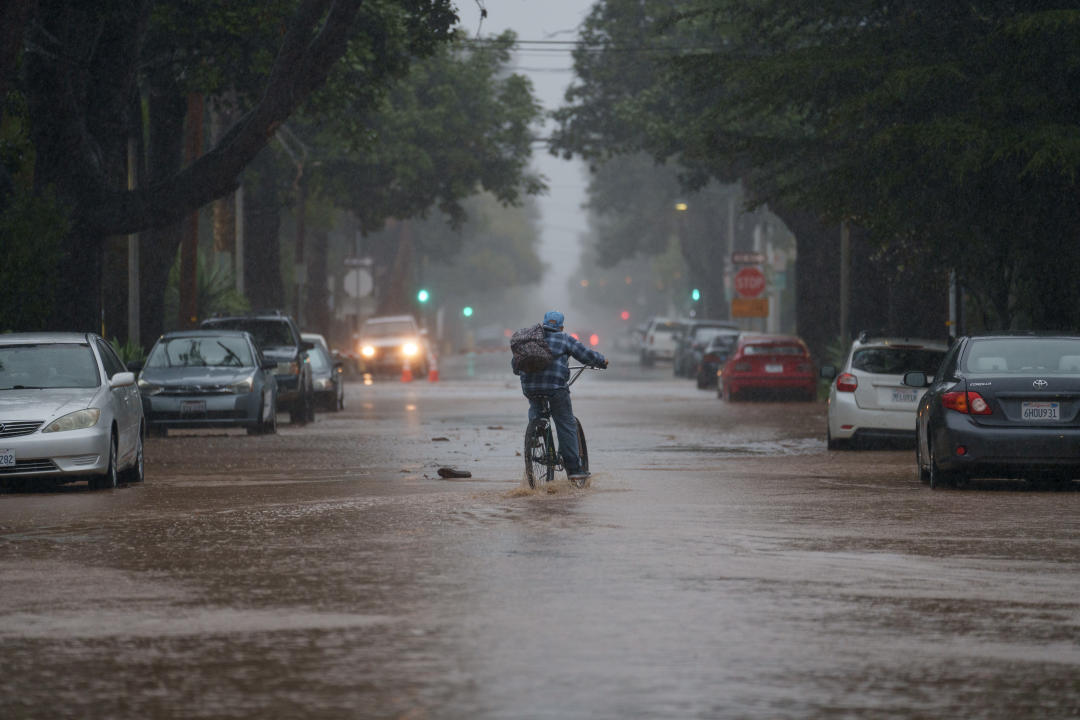 A person rides a bike through floodwater in Santa Barbara, Calif.