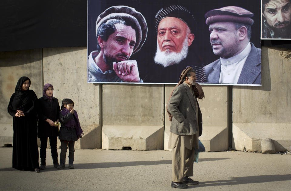 Afghan people wait for a bus next to a blast wall decorated with pictures of late Afghan politicians Ahmad Shah Massoud, Burhanuddin Rabbani and Afghanistan's Vice President Mohammed Qasim Fahim, from left to right, in the center of Kabul, Afghanistan, Monday, March 10, 2014. Afghanistan's influential Vice President Fahim, a leading commander in the alliance that fought the Taliban who was later accused with other warlords of targeting civilian areas during the country's civil war, died March 9, 2014. He was 57. (AP Photo/Anja Niedringhaus)