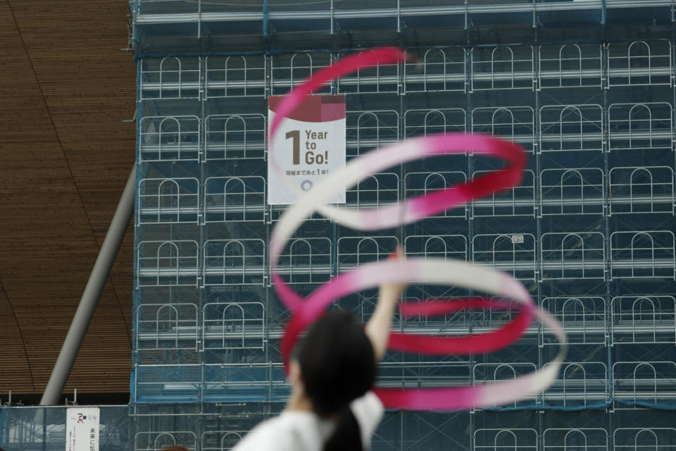 Former Japanese Olympic gymnast Kotono Tanaka performs as a "1-Year to Go" banner hangs outside the Ariake Gymnastics Center, Monday, July 22, 2019, in Tokyo. Despite scandals, rising costs and doubts about the economic payoff, the Tokyo Olympics will be a must-see event — if you can find a ticket or a hotel room — when they open in a year. Tokyo was supposed to be a "safe pair of hands" after Rio de Janeiro's corruption and near-meltdown three years ago. (AP Photo/Jae C. Hong)