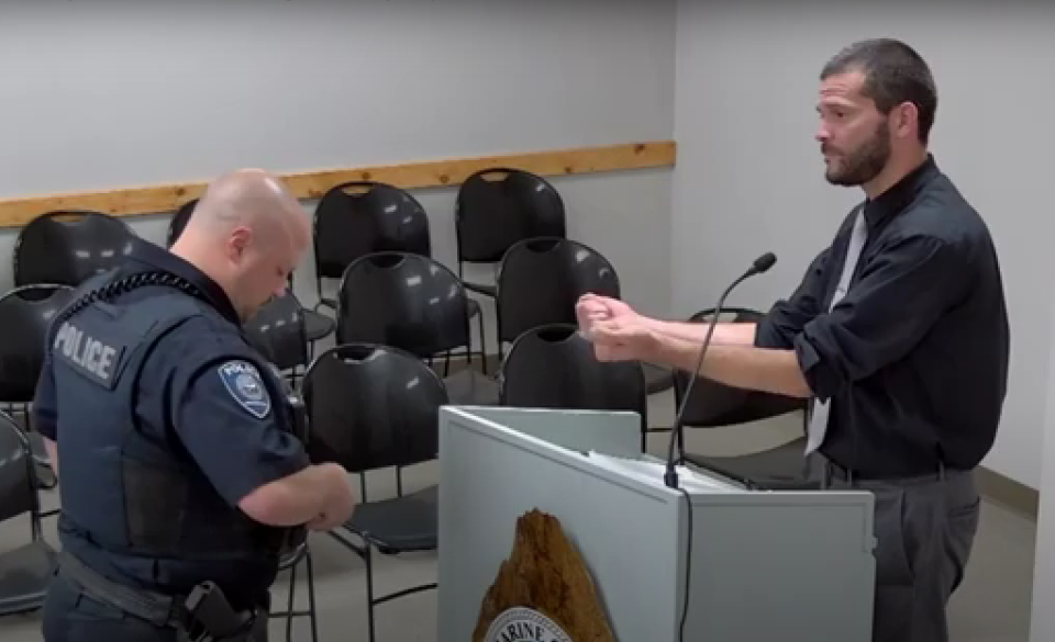 Marine City Commissioner Mike Hilferink holds his hands out to be handcuffed after refusing to leave the public comment podium a commission meeting on Thursday, Sept. 7, 2023. Officials told Hilferink it was against procedure for him to respond to residnets' comments during that period rather than reserve remarks at the end of the meeting during commissioner privilege.