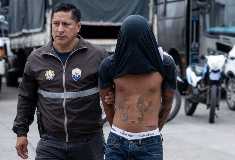 Un agente de la Policía Nacional de Ecuador escolta a uno de los varios presuntos miembros de la banda criminal 