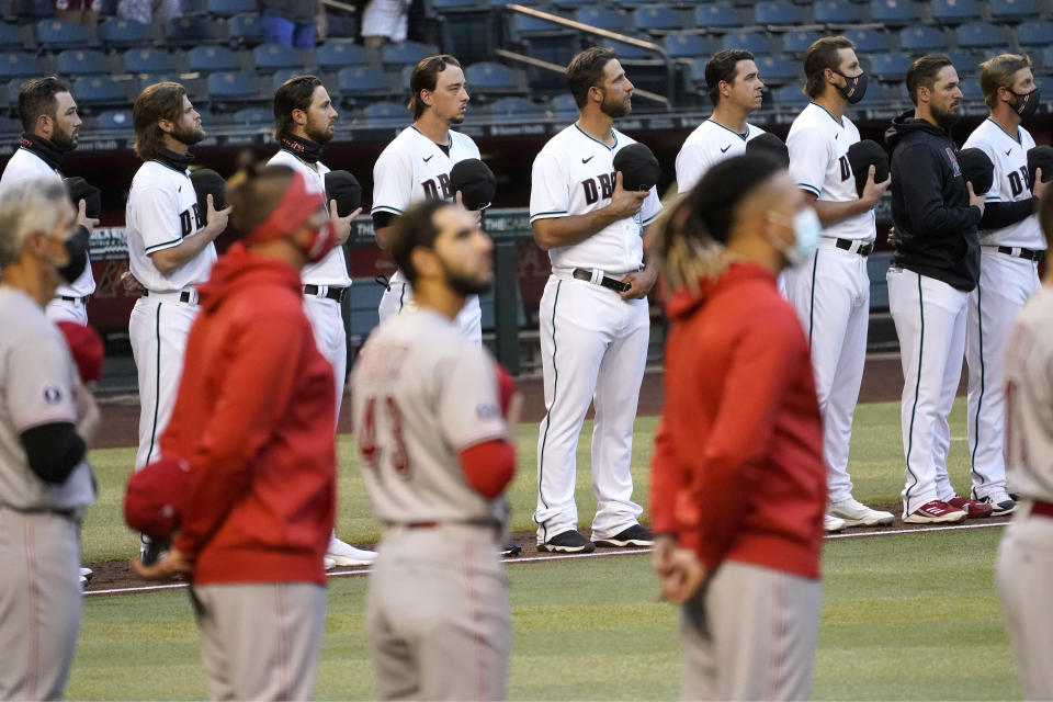 Arizona Diamondbacks and Cincinnati Reds players stand for the national anthem prior to a baseball game, Friday, April 9, 2021, in Phoenix. (AP Photo/Matt York)