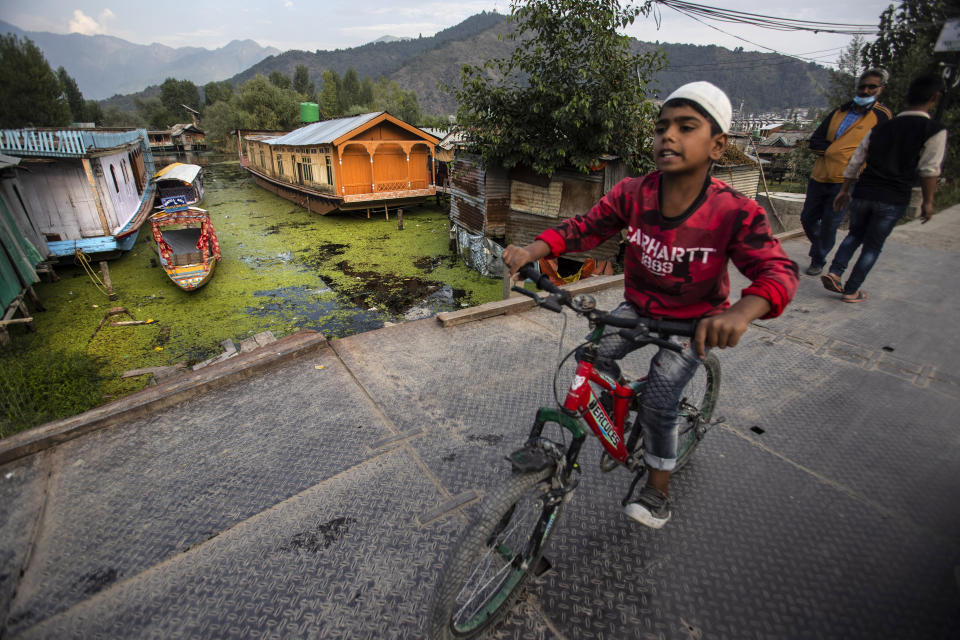 A Kashmiri child crosses a bridge over the Dal Lake in Srinagar, Indian controlled Kashmir, Saturday, Aug. 28, 2021. Weeds, silt and untreated sewage are increasingly choking the sprawling scenic lake, which dominates the city and draws tens of thousands of tourists each year. (AP Photo/Mukhtar Khan)