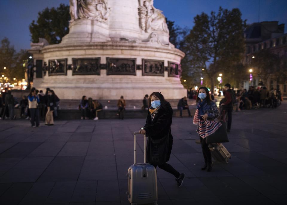 Tourists wearing protective masks walk on Republique square in Paris, Thursday, Oct. 29, 2020. France prepared to shut down again for a month to try to put the brakes on the fast-moving coronavirus. Schools are allowed to remain open in this new lockdown, which is gentler than what France saw in the spring. But still a shock to restaurants and other businesses ordered to close their doors in one of the world's biggest economies.(AP Photo/Lewis Joly)