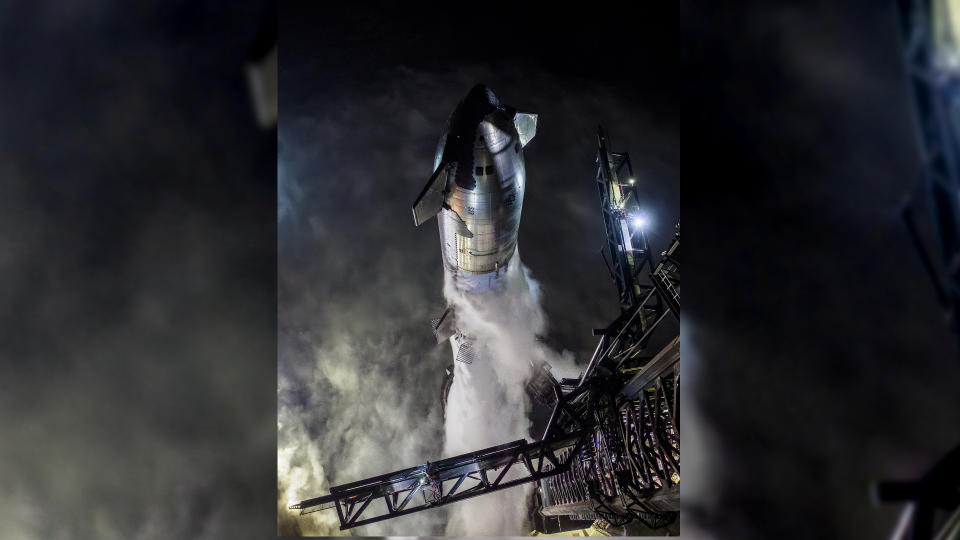 A Starship Flight 3 rocket and Super Heavy booster atop the launch pad at night in a fueling test