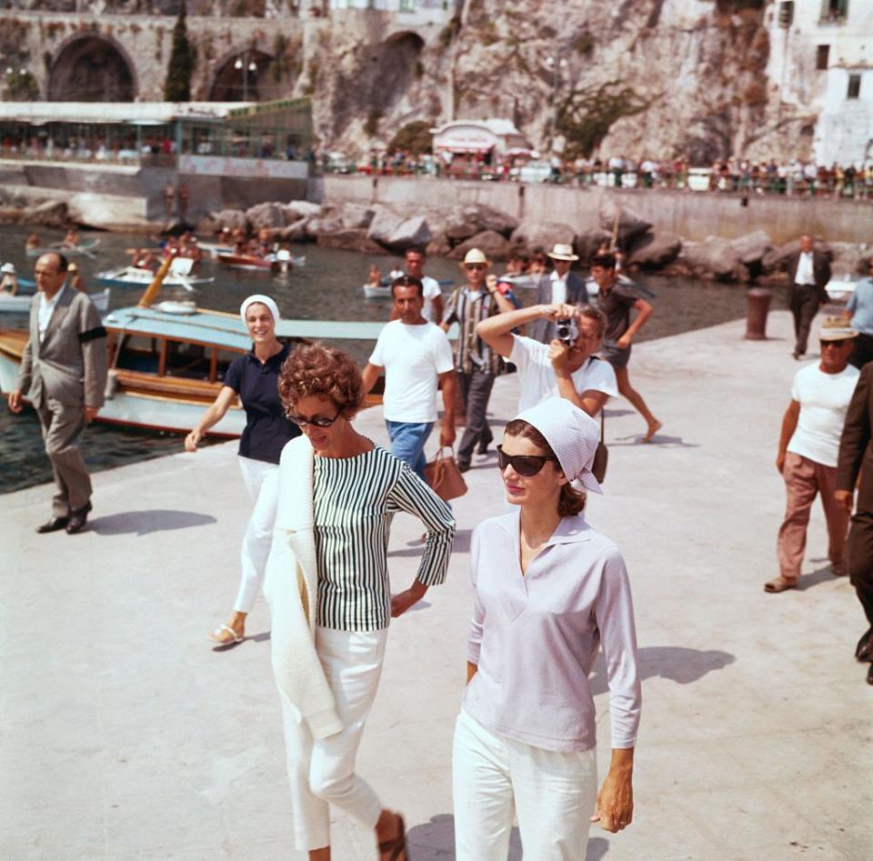 <p>Wearing a kerchief, collared sweater, and white pants, Jackie Kennedy strolls in Amalfi during a holiday on the Mediterranean coast with Marella Agnelli.<br></p>
