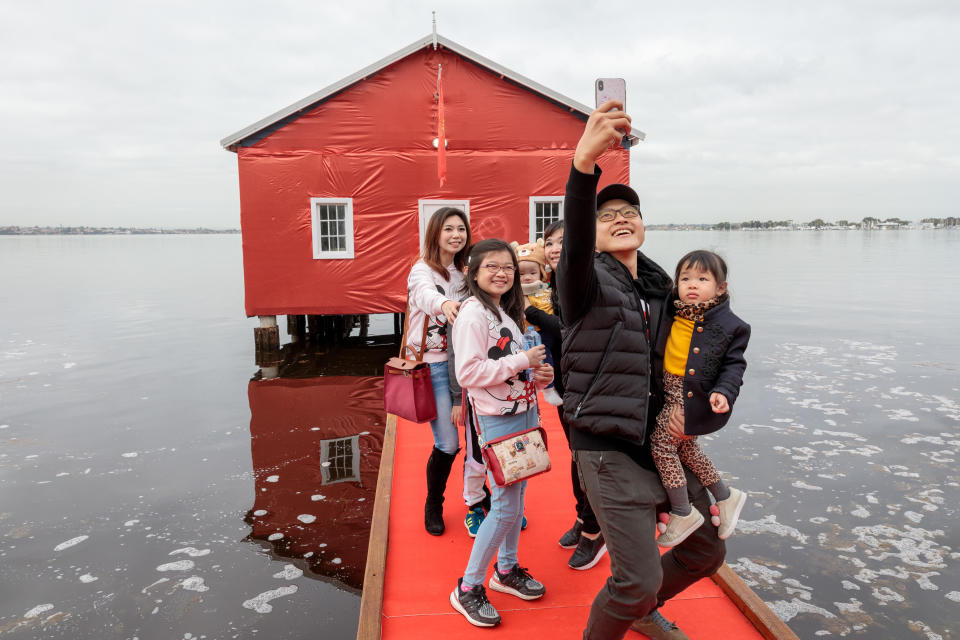 Members of the public take pictures of the Crawley boatshed on the Swan river which has been covered in red to celebrate the arrival of Manchester United Football Club in Perth.