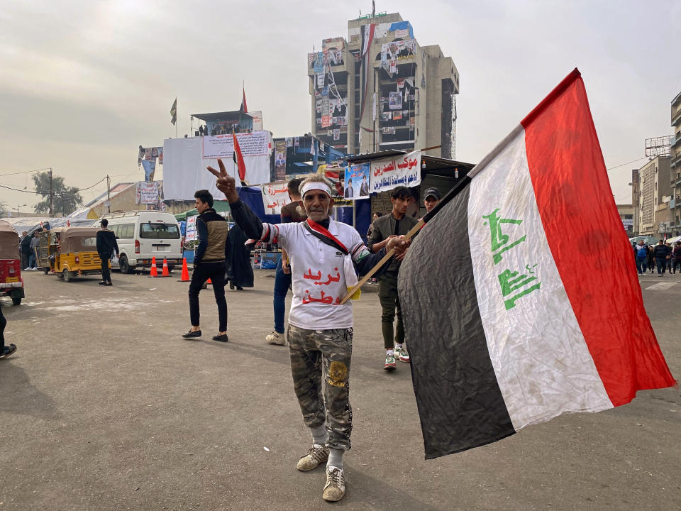 CORRECTS TO REMOVE REFERENCE TO INCIDENT INVOLVING GUNMAN - An anti-government protester poses for a picture while holding a national flag during ongoing protests in Baghdad, Iraq, Thursday, Dec. 12, 2019. The Arabic on his shirt reads, "We want a homeland." (AP Photo/Khalid Mohammed)