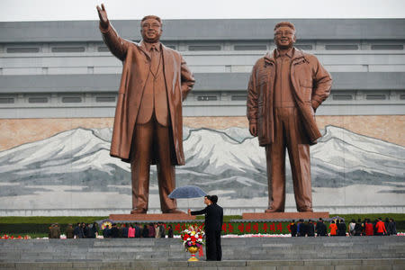 A man holds an umbrella over flowers as people gather to pay their respects at the statues of North Korea founder Kim Il Sung (L) and late leader Kim Jong Il in Pyongyang, North Korea April 14, 2017. REUTERS/Damir Sagolj