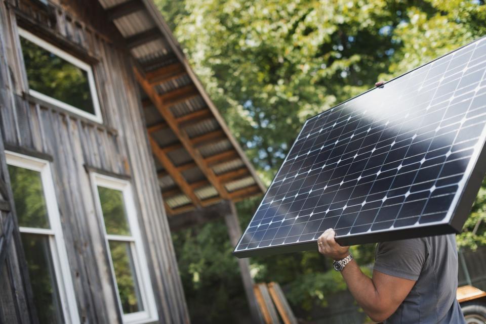 A man carrying a solar panel on a green construction site, working on a green building project.