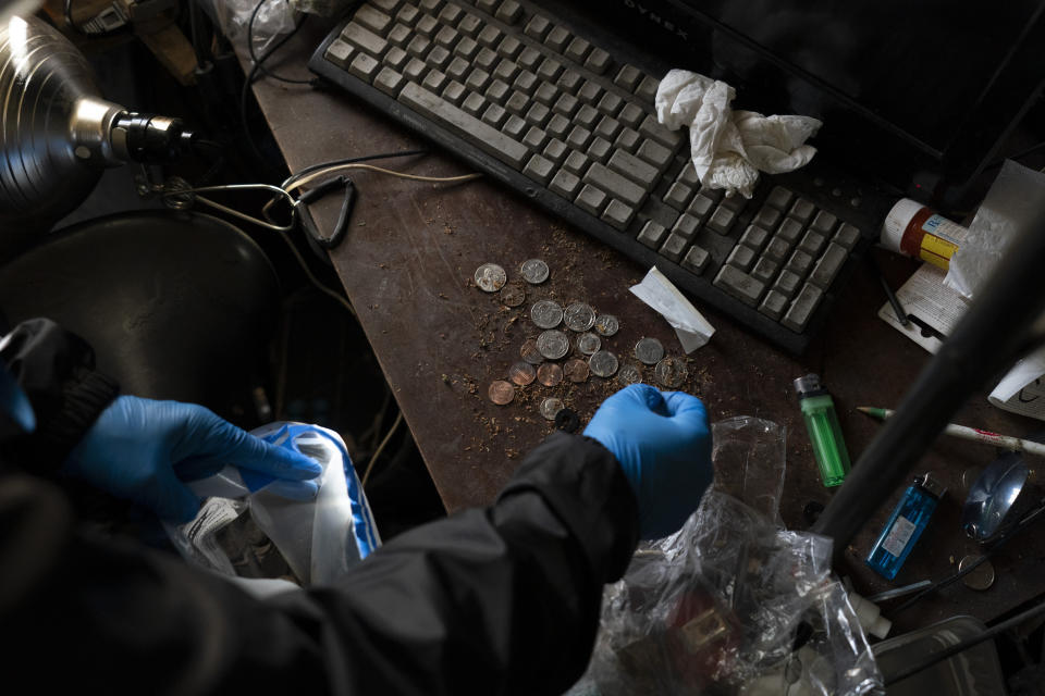 Arusyak Martirosyan, an investigator with the Los Angeles County Public Administrator's office, gathers up coins into a plastic bag during her search through a cluttered micro-apartment in Los Angeles, Wednesday, Dec. 13, 2023, where a tenant was found dead in his bed with no apparent next of kin. (AP Photo/Jae C. Hong)