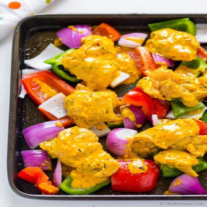 A baking sheet topped with marinated chicken, onions, and peppers