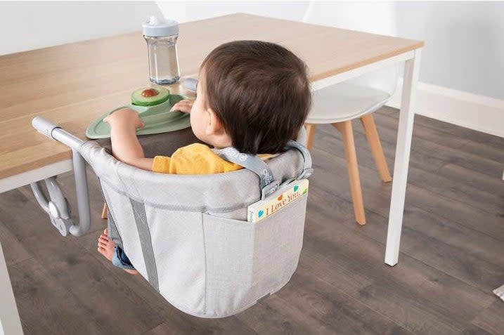 Toddler model in a portable high chair attached to a table, with food and drink in front of them