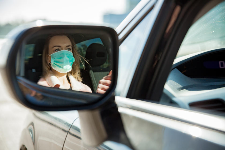 Woman in protective mask driving a car on road. Safe traveling.