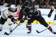 Arizona Coyotes defenseman Shayne Gostisbehere (14) tries to keep the puck away from Boston Bruins left wing Taylor Hall (71) during the first period of an NHL hockey game in Tempe, Ariz., Friday, Dec. 9, 2022. (AP Photo/Ross D. Franklin)