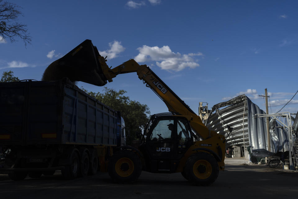 A transport truck is loaded with grain as a warehoused damaged in Russian missile attacks is seen in the background at a grain facility in Pavlivka, Ukraine, Saturday, July 22, 2023. (AP Photo/Jae C. Hong)