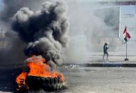 Iraqi demonstrator walks past burning tires as they block a road during the ongoing anti-government protest in Nassiriya