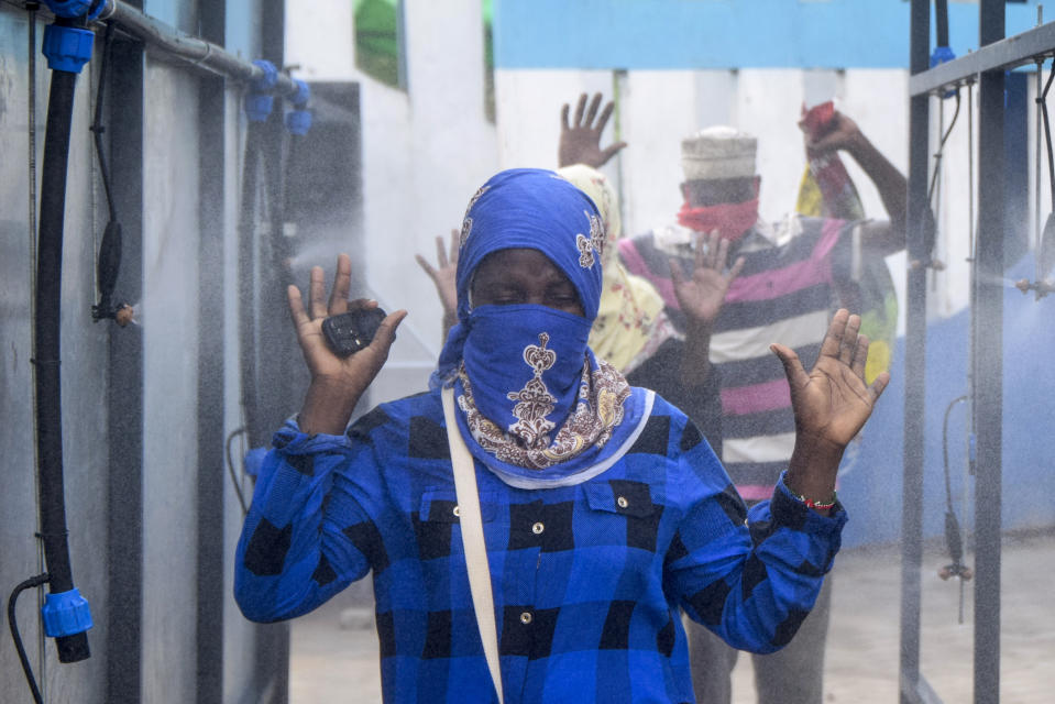 Ferry commuters walk through an automated disinfecting machine installed this week that sprays disinfectant onto all passengers boarding or disembarking ferries that cross the harbor of Mombasa, on the south coast of Kenya Wednesday, April 8, 2020. Kenya this week increased its restrictions to combat the coronavirus, announcing travel bans into and out of the capital city, Nairobi, the port of Mombasa and two counties. (AP Photo)