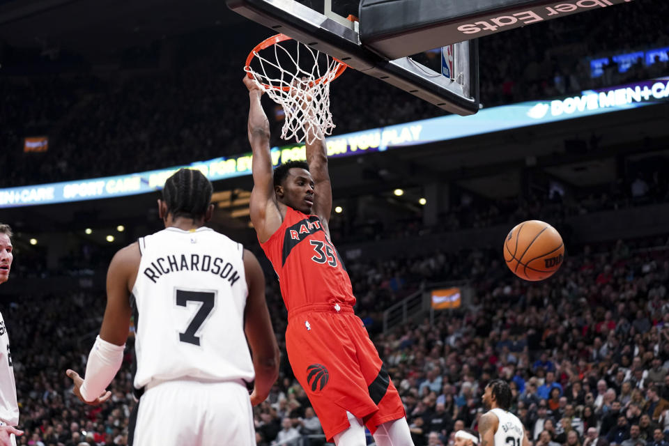 Toronto Raptors forward Christian Koloko (35) hangs on the rim after dunking next to San Antonio Spurs guard Josh Richardson (7) during the first half of an NBA basketball game Wednesday, Feb. 8, 2023, in Toronto. (Arlyn McAdorey/The Canadian Press via AP)