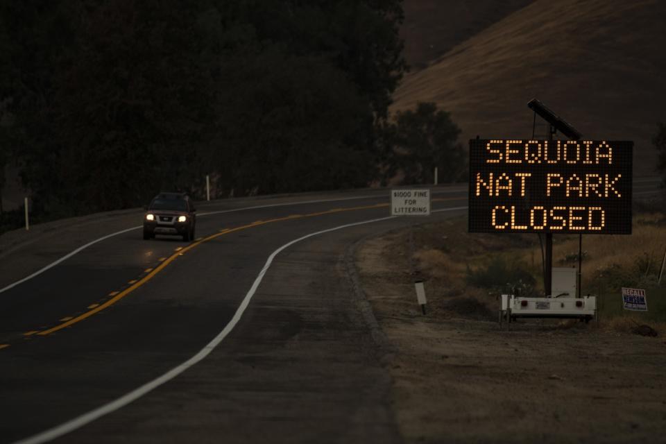 A car with headlights on drives away from a message sign announcing the closure of Sequoia National Park