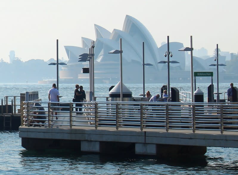 Commuters wait for a ferry as smoke from bushfires shrouds the Sydney Opera House in Sydney