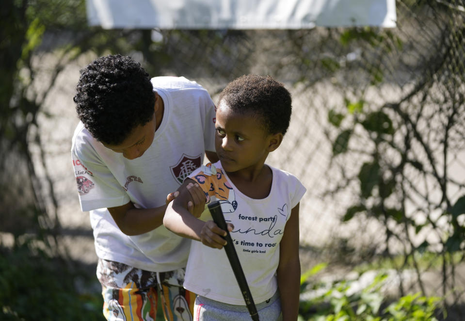 CORRECTS CADDIE'S SURNAME - A boy helps a girl into a proper golf stance on the grounds of the Nusacquilombo cultural center where children are learning the basics from caddie Marcelo Modesto, in Cidade de Deus or City of God favela, in Rio de Janeiro, Brazil, Thursday, Dec. 9, 2021. Modesto from one of Rio's poorest neighborhoods works at one of the seaside city's most exclusive golf courses, earning a comfortable living guiding wealthy patrons around the fairways and greens of the course. Now he is sharing his golf skills with kids from his favela. (AP Photo/Silvia Izquierdo)