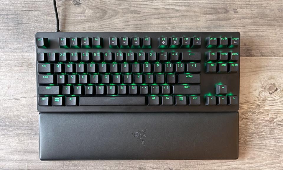 The Razer Huntsman V2 TKL gaming keyboard + wrist rest sits on a light brown wooden table.