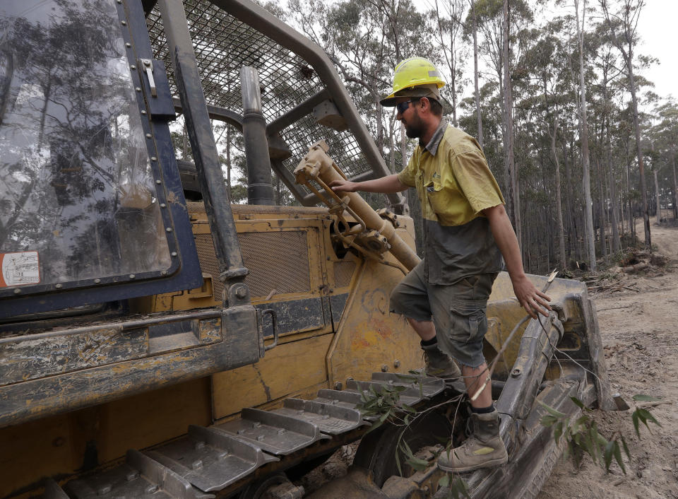 A bulldozer operator that goes by the name "Emu" climbs on his dozer as he works at building a containment line at a fire near Bodalla, Australia, Sunday, Jan. 12, 2020. Authorities are using relatively benign conditions forecast in southeast Australia for a week or more to consolidate containment lines around scores of fires that are likely to burn for weeks without heavy rainfall. (AP Photo/Rick Rycroft)