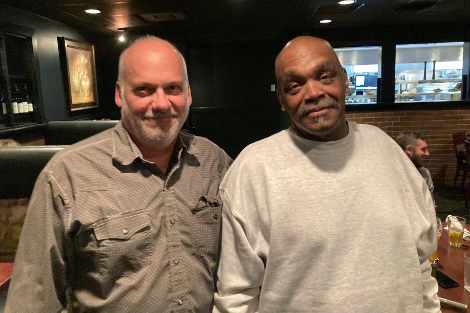 In this photo provided by James Comstock, John Lewis, left, stands with Jesse Johnson at a restaurant in Lake Oswego, Ore., Tuesday, Sept. 5, 2023. Johnson, convicted of a 1998 murder and sentenced to death, is now free, two years after the Oregon Court of Appeals reversed the conviction. Prosecutors asked for the case to be dismissed, saying that with the passage of time, the state no longer believes that it can prove Johnson was guilty. Johnson has always maintained his innocence.