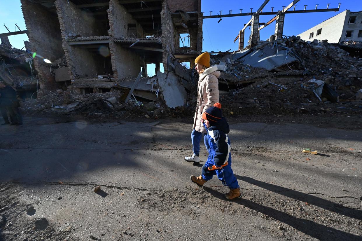 A local resident hold the hand of a child as they walk past a destroyed building following a C-300 missile strike on the Ukrainian city of Kharkiv on 31 March 2023 (AFP via Getty Images)