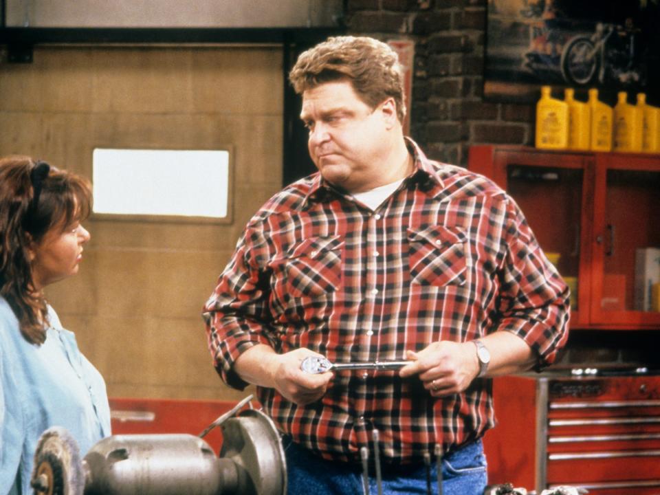 John Goodman wearing a red, white, and black checkered shirt as Dan Conner on "Roseanne."