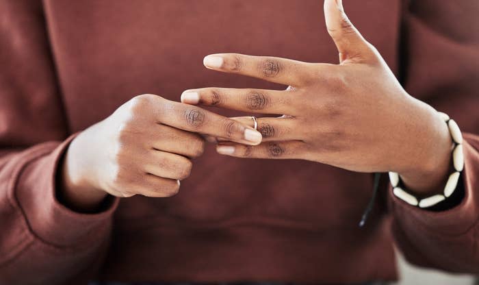 Person wearing a long-sleeve shirt and bracelet, using their right hand to remove a ring from their left hand