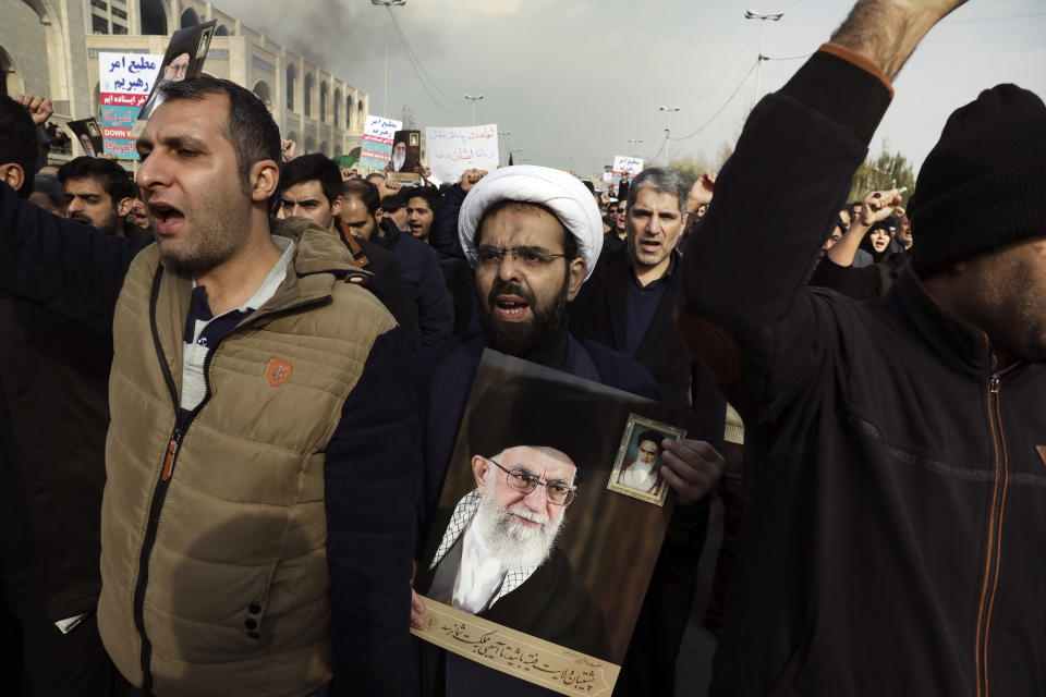 A cleric holds a poster of Iranian Supreme Leader Ayatollah Ali Khamenei and late revolutionary founder Ayatollah Khomeini, top right, while chanting slogans in a demonstration over the U.S. airstrike in Iraq that killed Iranian Revolutionary Guard Gen. Qassem Soleimani in Tehran, Iran, Jan. 3, 2020. Iran has vowed "harsh retaliation" for the U.S. airstrike near Baghdad's airport that killed Tehran's top general and the architect of its interventions across the Middle East, as tensions soared in the wake of the targeted killing. (AP Photo/Vahid Salemi)