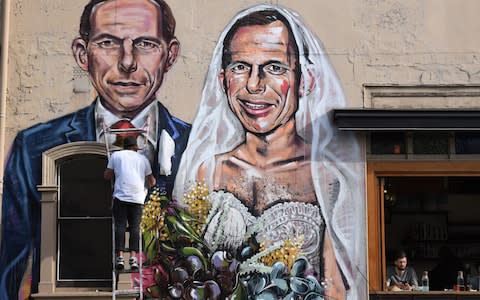 Artist Scott Marsh finishing off his mural of former Australian prime minister Tony Abbott getting married to himself at Hunters Corner in Redfern Sydney - Credit:  AAP