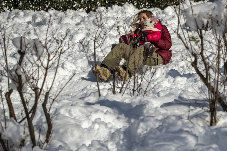 A woman child enjoy the snow in downtown Madrid, Spain, Sunday, Jan. 10, 2021. A large part of central Spain including the capital of Madrid are slowly clearing snow after the country's worst snowstorm in recent memory. (AP Photo/Manu Fernandez)