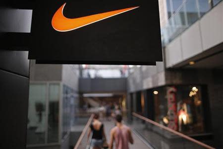 People walks past a Nike shop under the company logo at the Sanlitun shopping area in central Beijing, August 8, 2013. REUTERS/Petar Kujundzic